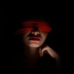 نمای هنری از زنی با چشم‌بند قرمز در نور کم، نمادی از بازی توافقی BDSM
