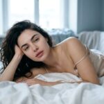 زنی در نور خنثای صبح میان خواب و بیداری روی ملحفهٔ ابریشمی سفید، نمادی از مرحلهٔ گذار خواب و خلاقیت