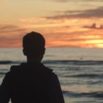 Silhouette of a teenager on a beach at sunset, back view