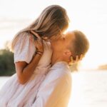 What Kissing Reveals About Real Intimacy in a Relationship بوسهٔ رمانتیک زوجی در غروب ساحل با نور گرم و روشن