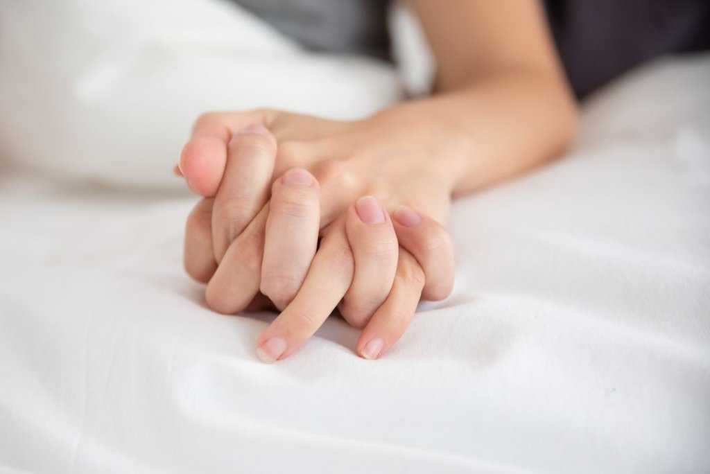 Intertwined hands of a couple on white bed sheets, intimacy after childbirth