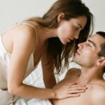 Sleep and Sexual Desire: What One Extra Hour Changes A couple in bed in morning light, she leaning over him with her hand on his chest — sleep and sexual desire