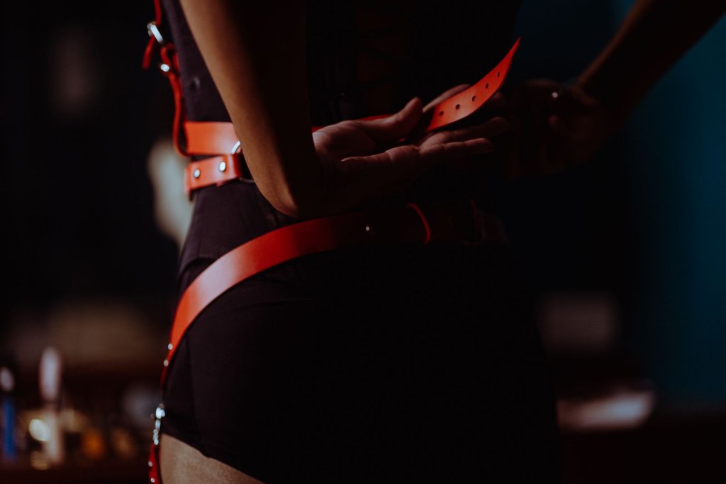 Woman in a black corset and red leather harness, illustrating consensual kink and BDSM in couples