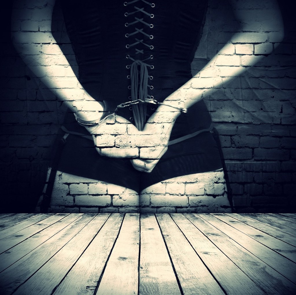 زن با کرست مشکی و دست‌های بسته با دستبند پشت کمر؛ نمادی از نقش مطیع در BDSM توافقی