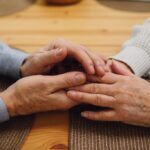 Close-up of an elderly couple holding hands on a wooden table, a sign of lasting closeness