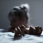 Moody close-up of a woman resting with her hands on a bed in soft grey light