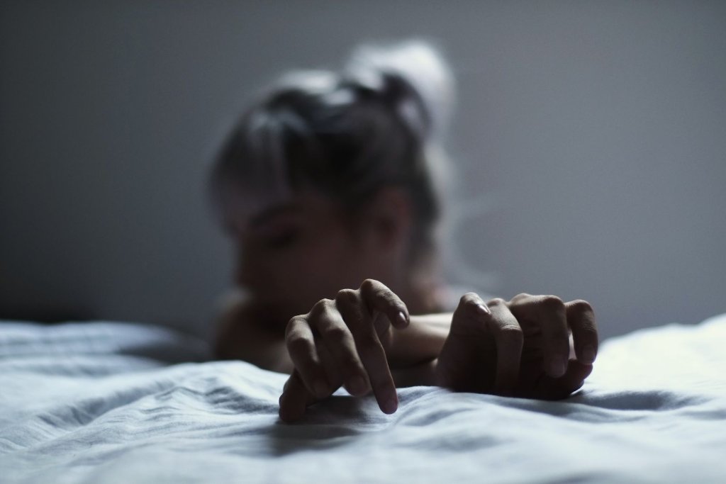 Moody close-up of a woman resting with her hands on a bed in soft grey light
