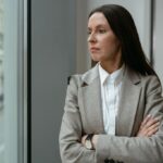 مدیر زن با کت خاکستری کنار پنجره در فکر؛ کمال‌گرایی مدیران و فرسودگی