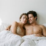 پورن و اختلال نعوظ؛ مقصر تماشاست یا رابطه با آن؟ Attractive young couple relaxed in bed in morning light, phones face-down — porn and erectile dysfunction in young men