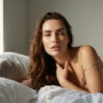 Woman lying in bed in soft afternoon light with a calm sensual expression, an image about mindfulness and sexual wellbeing